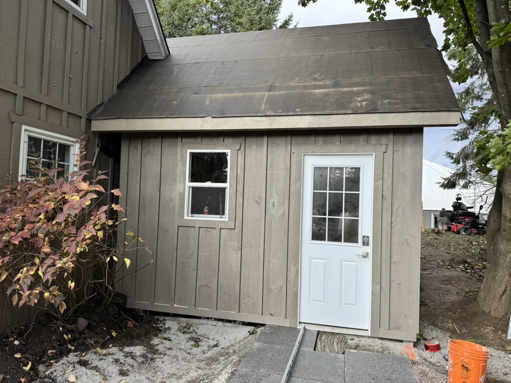 Grey board-and-batten shed with a white door and window