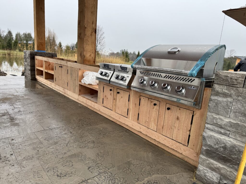 Outdoor kitchen run with a stainless grill, wood cabinets and stone end walls